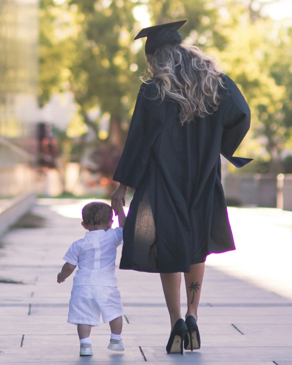 A mother in a grad gown walking with her young child